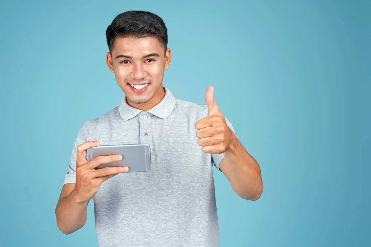 Man Gesturing Thumb Up with Smartphone on Blue Background